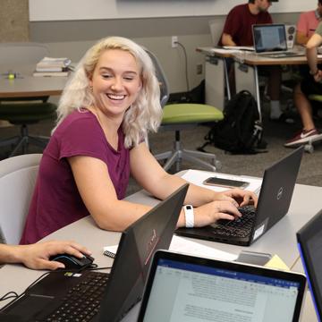 一个学生微笑着看着另一个学生的电脑屏幕.