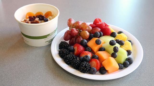 一张健康早餐的照片，上面有一盘水果和一杯燕麦片